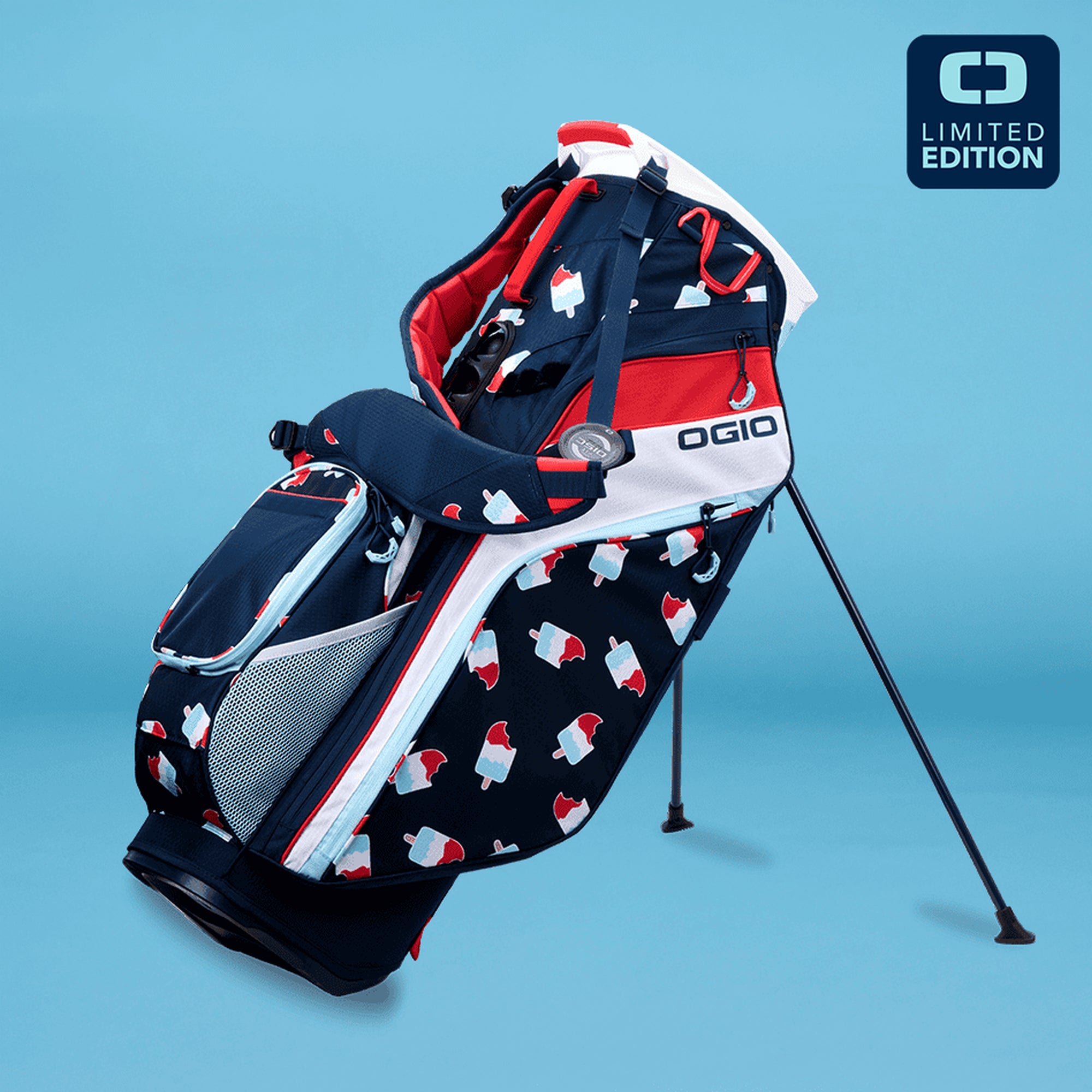 OGIO branded limited edition stand golf bag with a geometric pattern in red, white, and blue colors, displayed on a stand against a blue background.